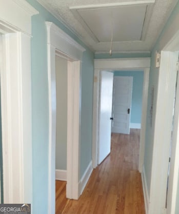 hallway featuring baseboards, wood finished floors, and attic access