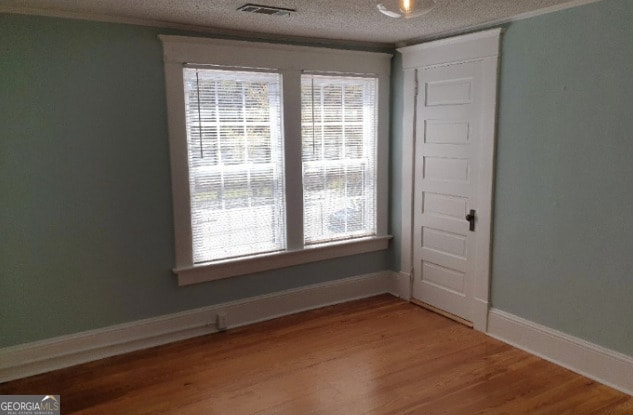 spare room featuring visible vents, a textured ceiling, baseboards, and wood finished floors