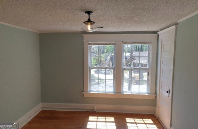 unfurnished dining area with a textured ceiling, visible vents, crown molding, wood finished floors, and baseboards
