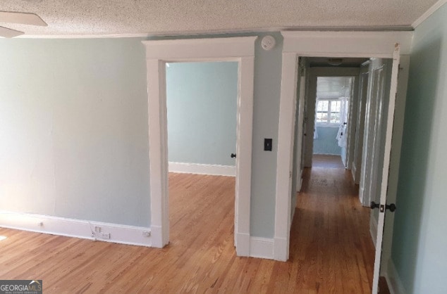corridor with crown molding, a textured ceiling, baseboards, and wood finished floors