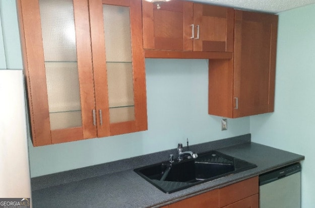 kitchen with white dishwasher, dark countertops, brown cabinetry, and a sink