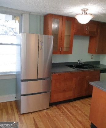 kitchen featuring brown cabinetry, freestanding refrigerator, a textured ceiling, a sink, and light wood finished floors