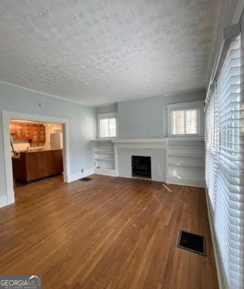 unfurnished living room with visible vents, wood finished floors, a fireplace, baseboards, and a textured ceiling