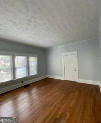 empty room featuring a textured ceiling, baseboards, and wood finished floors