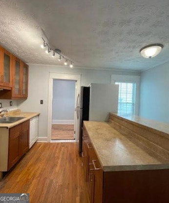 kitchen with white dishwasher, brown cabinetry, a sink, and wood finished floors