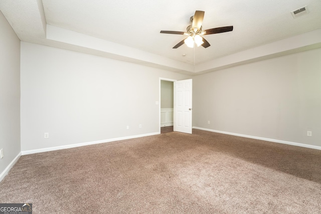 carpeted spare room featuring a ceiling fan, baseboards, visible vents, and a raised ceiling