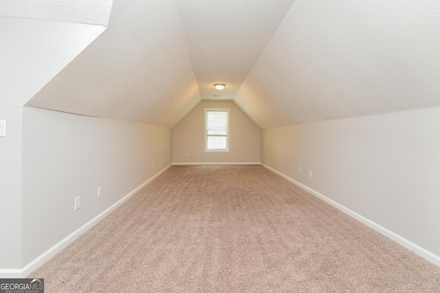 additional living space with baseboards, vaulted ceiling, a textured ceiling, and light colored carpet