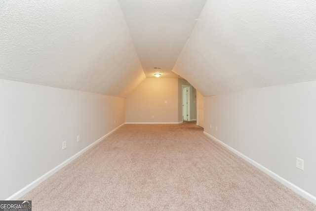 additional living space featuring baseboards, a textured ceiling, vaulted ceiling, and light carpet