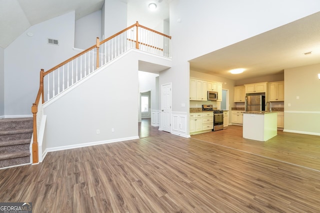 unfurnished living room featuring a high ceiling, stairs, light wood-style flooring, and visible vents