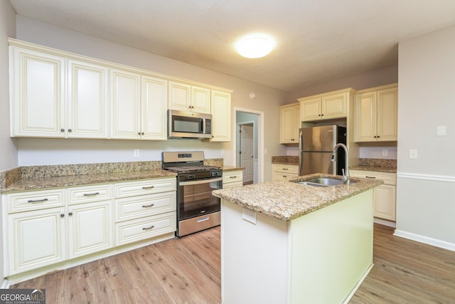 kitchen with appliances with stainless steel finishes, light stone counters, a sink, light wood-style flooring, and cream cabinetry