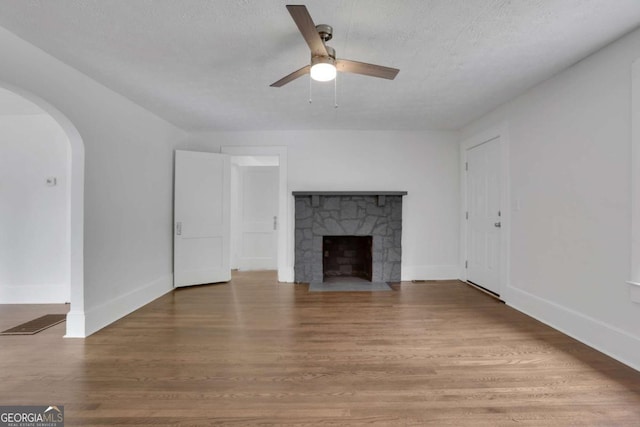 3223 Cleveland Hwy, Gainesville, GA 30506 - unfurnished living room featuring ceiling fan, arched walkways, a textured ceiling, a stone fireplace, and wood finished floors