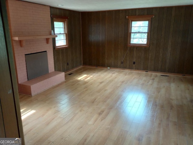 unfurnished living room with a brick fireplace, wooden walls, visible vents, and light wood-style floors