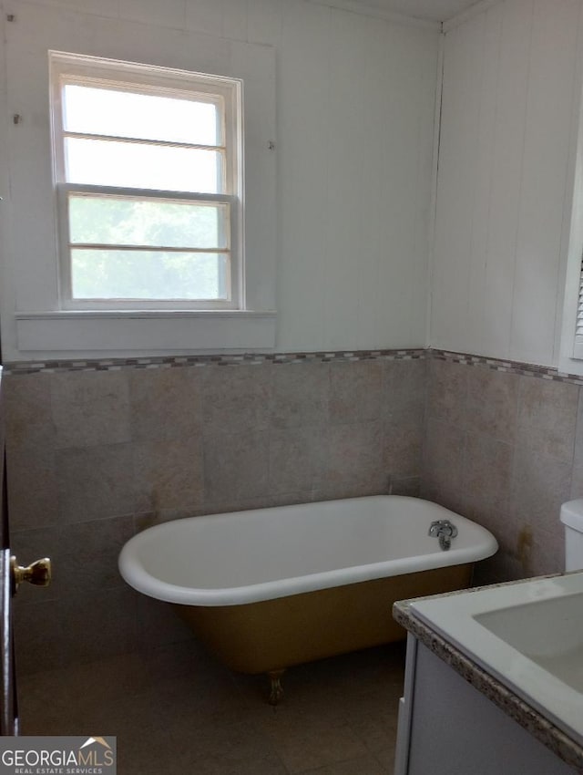 full bath featuring a freestanding bath, tile walls, tile patterned flooring, vanity, and a wainscoted wall
