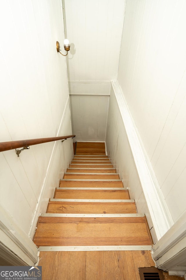 staircase with a decorative wall, visible vents, and wood finished floors