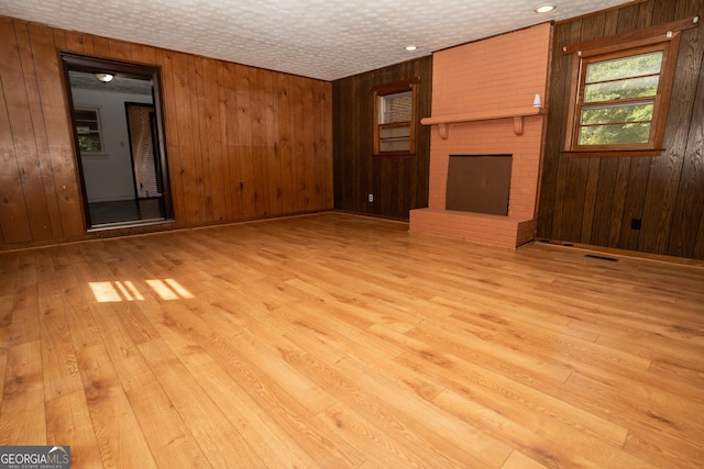 unfurnished living room featuring a fireplace, wooden walls, wood-type flooring, and visible vents