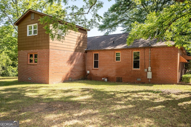 rear view of property with a yard, brick siding, crawl space, and roof with shingles