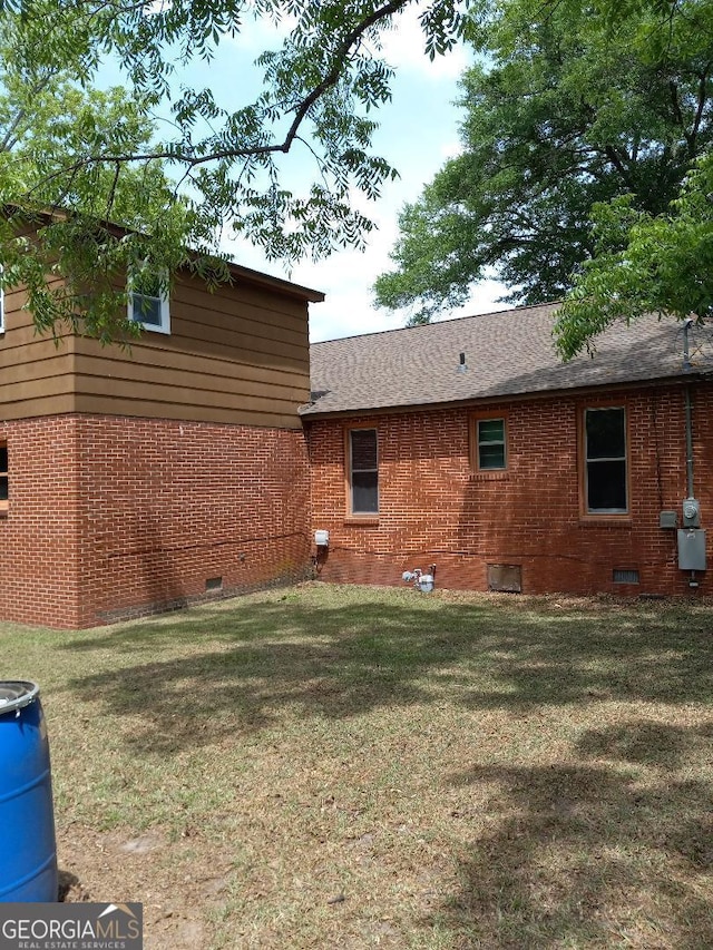 view of side of home with brick siding, a yard, and crawl space