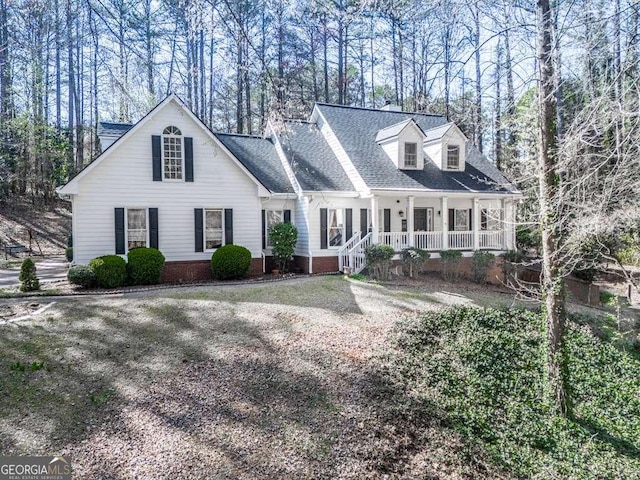 cape cod-style house featuring a shingled roof and covered porch