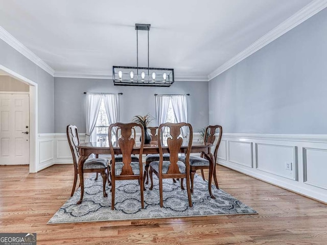 dining area with crown molding, a notable chandelier, a decorative wall, a wainscoted wall, and light wood-type flooring