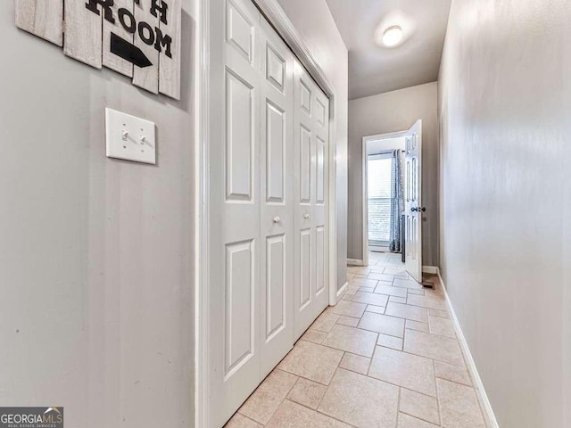 corridor with baseboards and stone tile floors