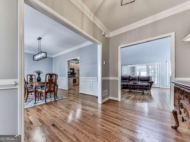 entrance foyer featuring wainscoting, wood finished floors, an inviting chandelier, ornamental molding, and a decorative wall