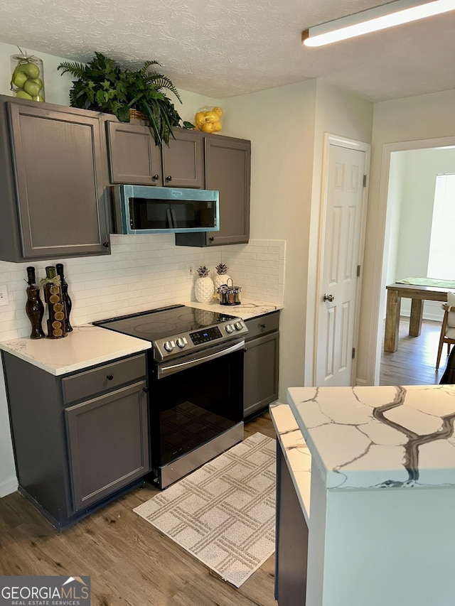 kitchen featuring decorative backsplash, gray cabinets, wood finished floors, and stainless steel appliances