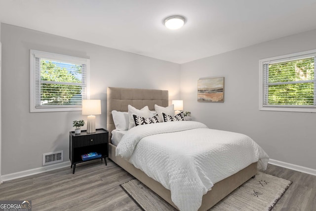 bedroom with baseboards, multiple windows, wood finished floors, and visible vents