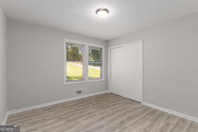 unfurnished bedroom with baseboards, visible vents, light wood finished floors, and a closet