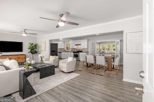 living room with crown molding, baseboards, ceiling fan, and wood finished floors