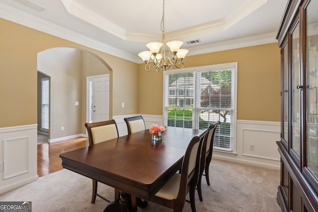 dining area with arched walkways, a chandelier, a raised ceiling, crown molding, and wainscoting