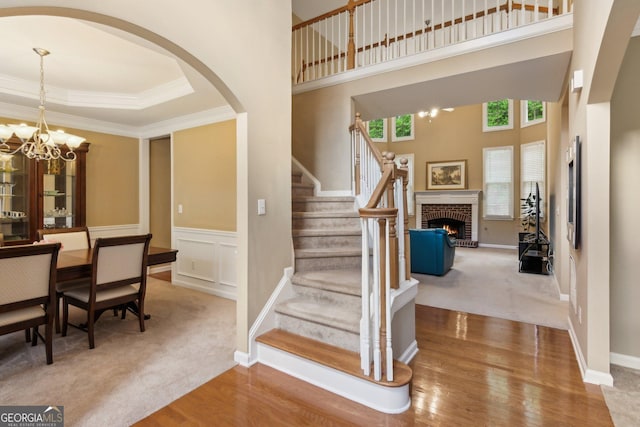 staircase featuring arched walkways, a fireplace, crown molding, wood finished floors, and a towering ceiling