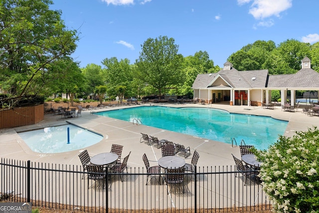community pool with fence, a patio, and view of scattered trees