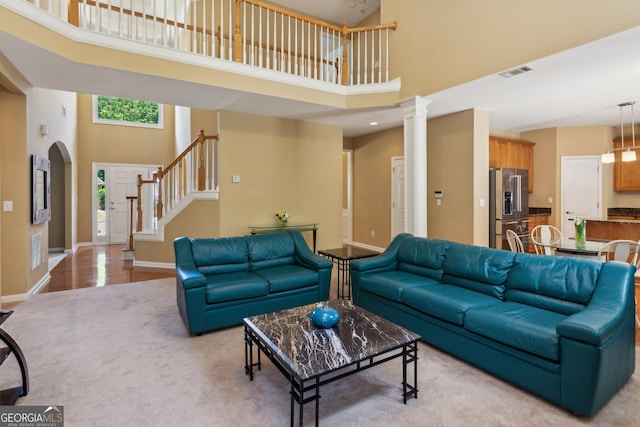living area with a towering ceiling, stairs, light colored carpet, baseboards, and arched walkways
