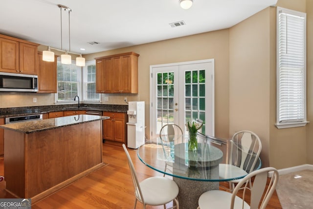 kitchen with stainless steel microwave, a sink, french doors, a kitchen island, and hanging light fixtures