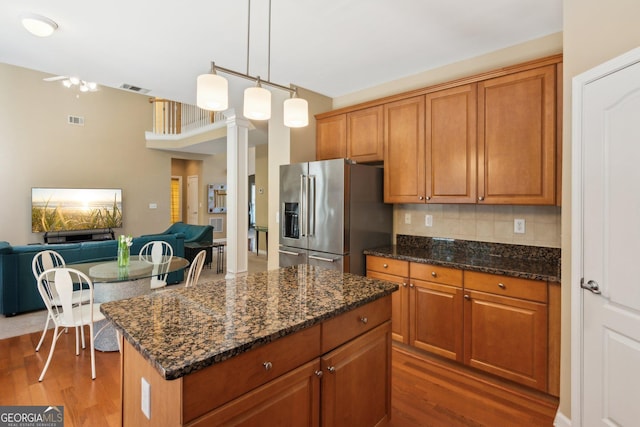 kitchen with high end refrigerator, dark wood-style floors, brown cabinets, backsplash, and dark stone counters