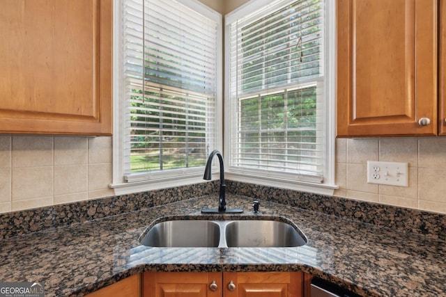 kitchen view of a sink, dark stone countertops, and decorative backsplash