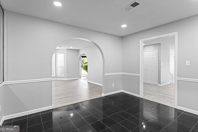 empty room featuring arched walkways, baseboards, recessed lighting, and visible vents