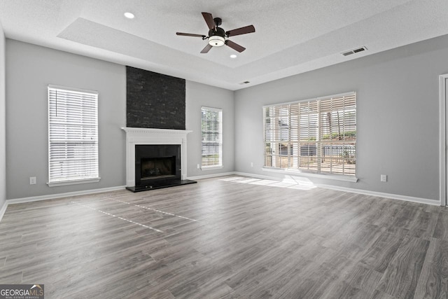 unfurnished living room featuring a ceiling fan, visible vents, a large fireplace, wood finished floors, and a raised ceiling
