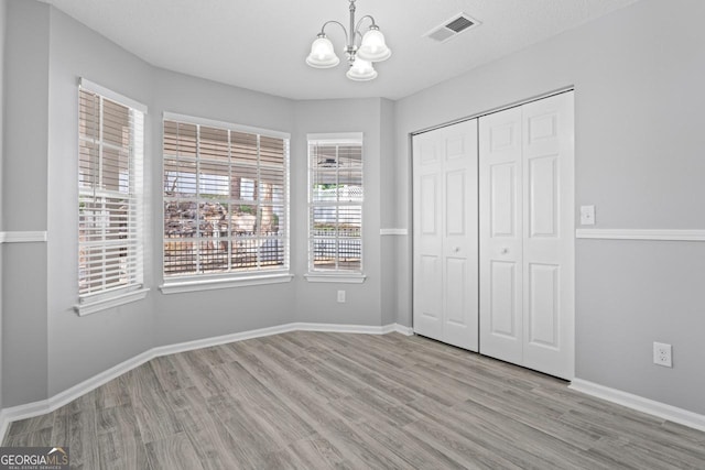 unfurnished bedroom with a chandelier, baseboards, wood finished floors, visible vents, and a closet