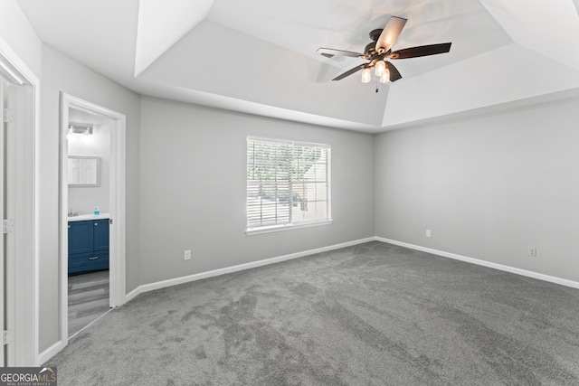 unfurnished bedroom featuring a tray ceiling, baseboards, ensuite bathroom, and carpet flooring