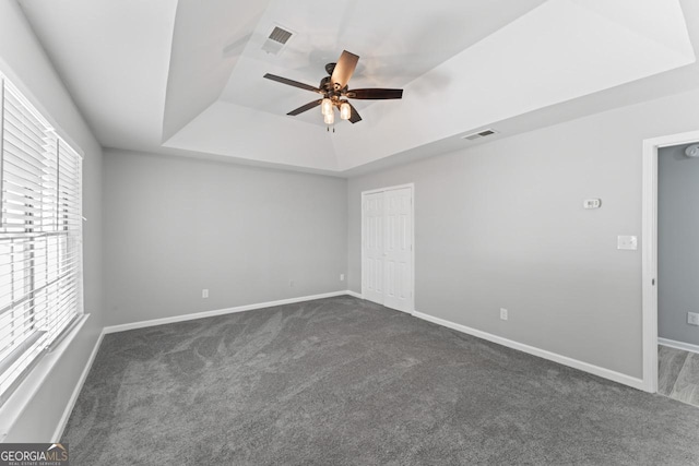 unfurnished room featuring a ceiling fan, visible vents, a raised ceiling, baseboards, and dark carpet