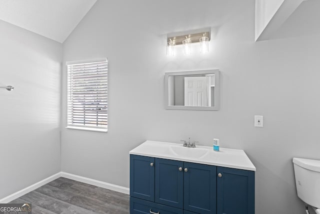 bathroom with wood finished floors, vanity, baseboards, toilet, and lofted ceiling