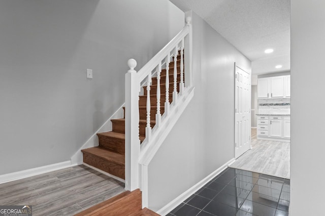 stairs featuring a textured ceiling, baseboards, recessed lighting, and wood finished floors
