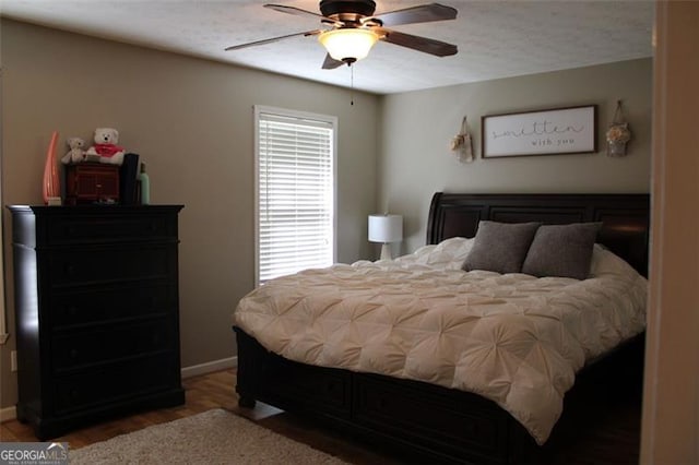 bedroom featuring baseboards, a ceiling fan, wood finished floors, and multiple windows