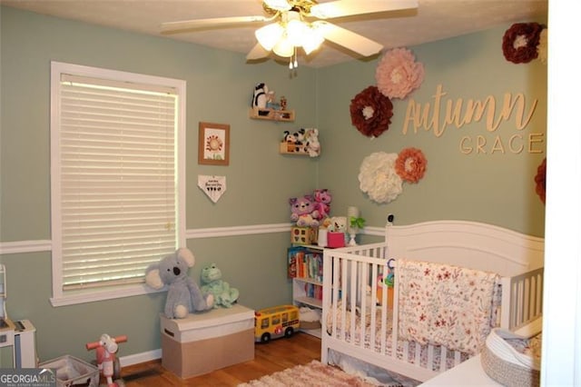 bedroom featuring a nursery area, a ceiling fan, and wood finished floors