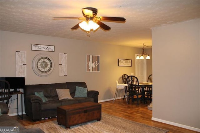 living area featuring a textured ceiling, baseboards, ceiling fan with notable chandelier, and wood finished floors