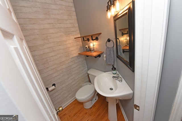 bathroom with a sink, wood finished floors, wooden walls, and toilet