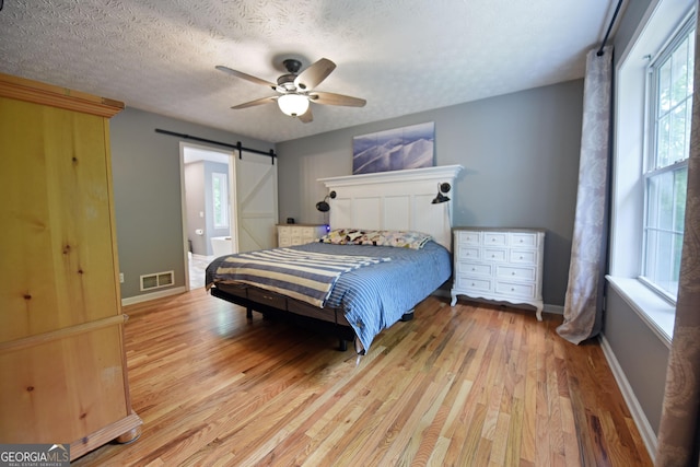 bedroom with visible vents, a barn door, multiple windows, and light wood-type flooring