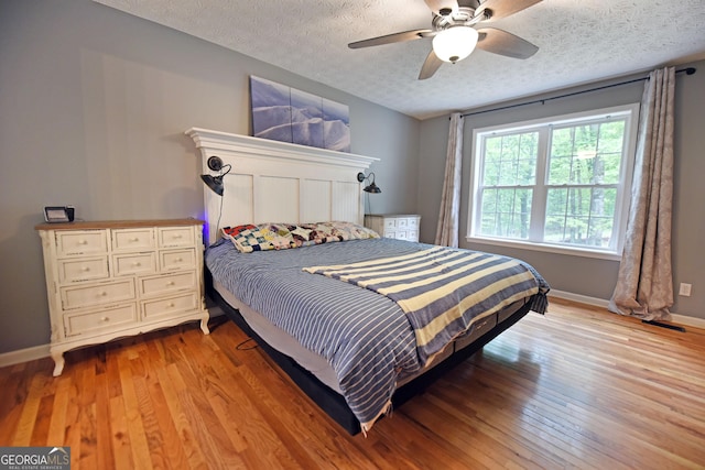 bedroom featuring baseboards, a ceiling fan, light wood finished floors, and a textured ceiling