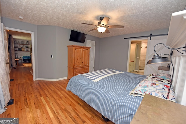 bedroom featuring a ceiling fan, a textured ceiling, a barn door, baseboards, and light wood finished floors